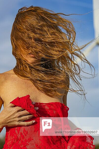Ein schönes rothaariges Model posiert im Freien mit Windrädern im Hintergrund