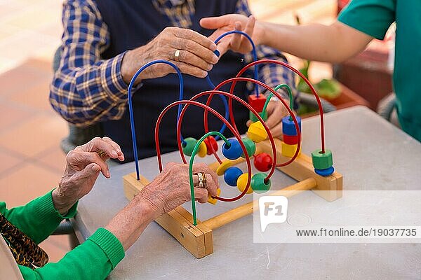 Die Hände zweier älterer Menschen im Garten eines Pflegeheims oder Seniorenheims  die mit Spielen zur Verbesserung der Beweglichkeit der Hände spielen