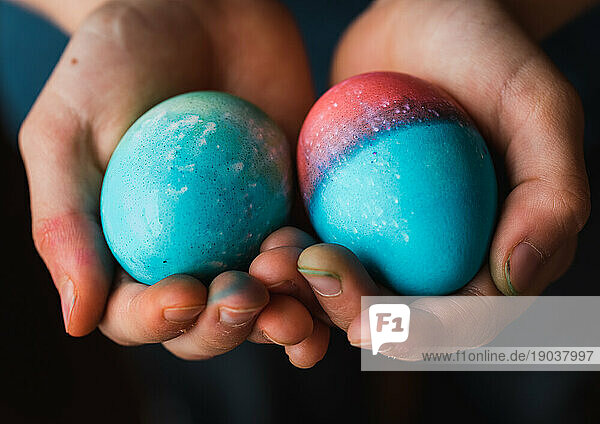 Close up of child's hands holding two colored Easter eggs.