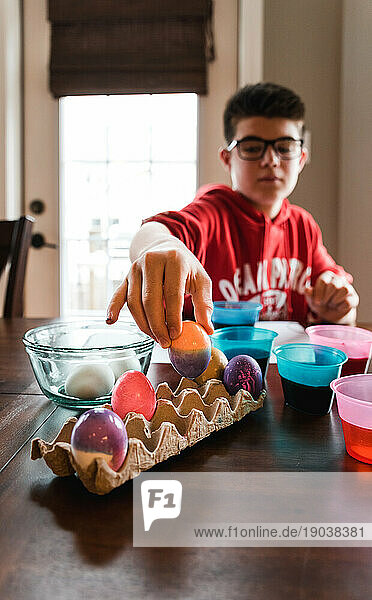 Boy placing colorful dyed Easter egg in a cardboard carton to dry.