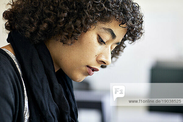 Close-up of thoughtful businesswoman with curly hair looking down in office