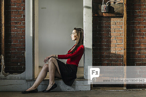 a young woman in a red top sits in a doorway in an industrial building