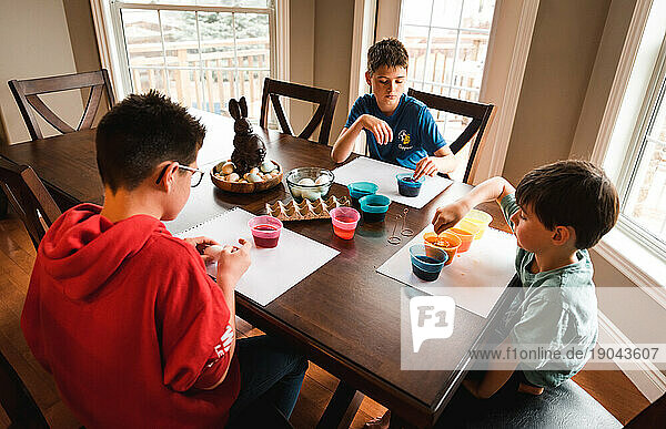 Three boys dying colorful Easter eggs at a wooden table together..