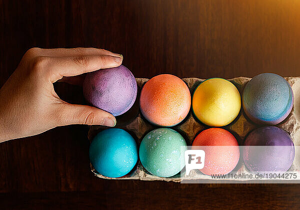 High angle of hand placing dyed egg with other colored Easter eggs.