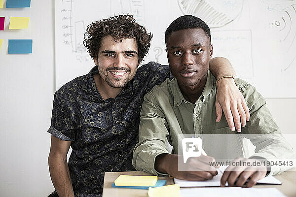 two young men studying on a table  looking to the camera