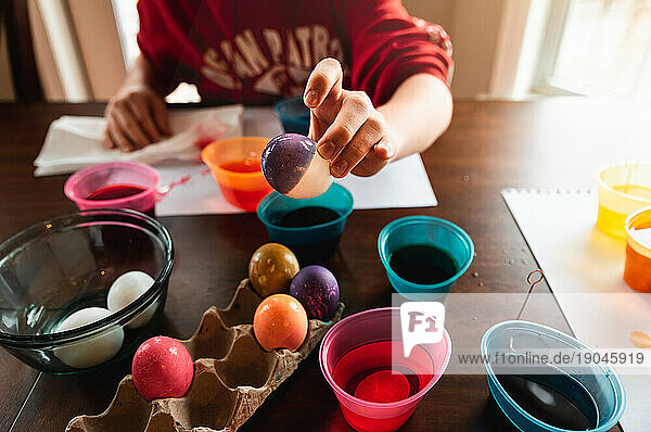 Crop of hand holding colored Easter egg with dye containers in back.