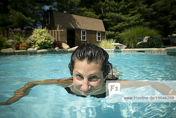 Woman submerged in swimming pool in backyard.