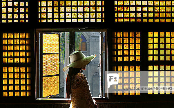 Woman in hat in hallway in front of capiz (shell) window in San Agustin Church  Manila  Philippines