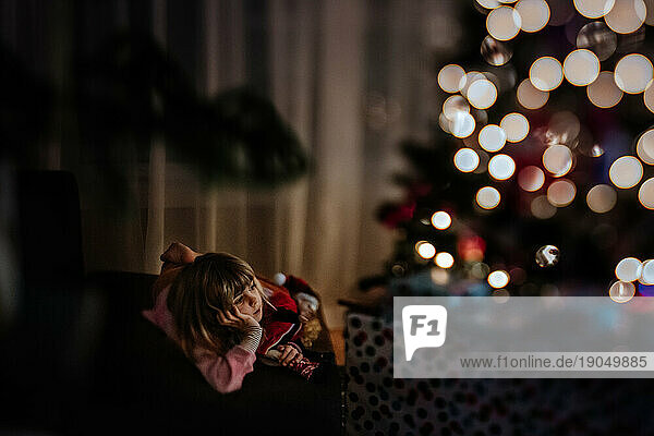 girl watching tv and cuddling her elf in front of the christmas tree