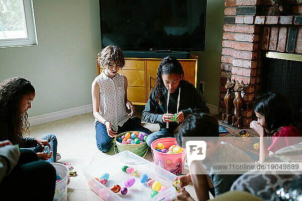 Kids sit together on the floor opening up their plastic Easter eggs