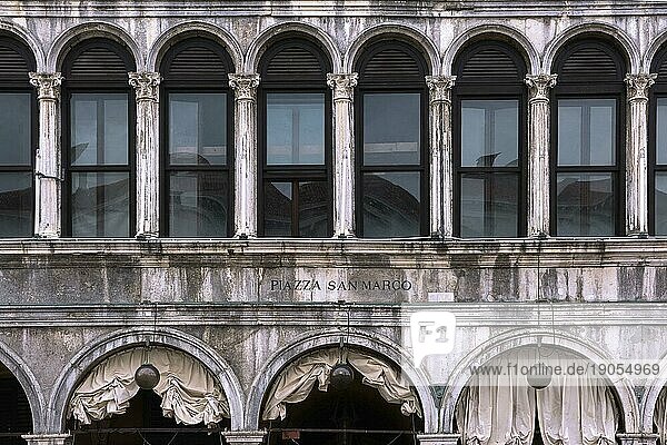 Frontalaufnahme der Fassade des Gebäudes der Procurate Vecchie auf dem Markusplatz  Venedig  Italien. Gleichmäßige Reihen von Arkaden und Fenstern im Stil der Renaissance  gealterter Stein  Inschrift auf Italienisch. Übersetzung  Markusplatz
