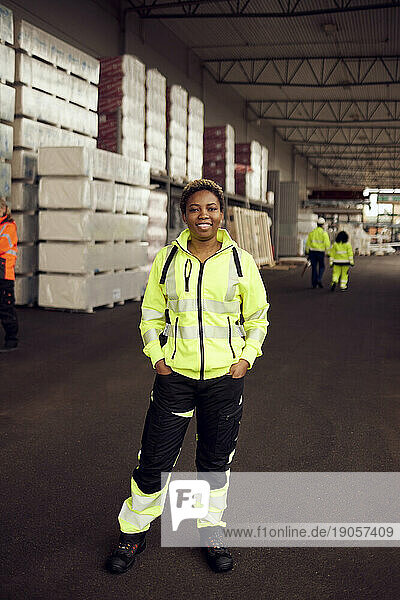 Porträt einer lächelnden Arbeiterin in reflektierender Kleidung  die in einer Fabrik steht