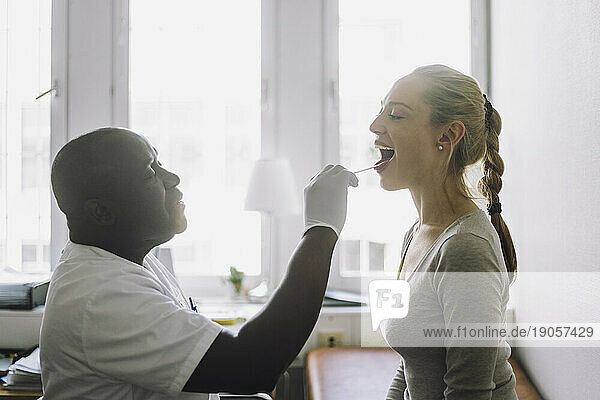 Seitenansicht eines männlichen Arztes  der den Mund einer Patientin in einer Klinik untersucht
