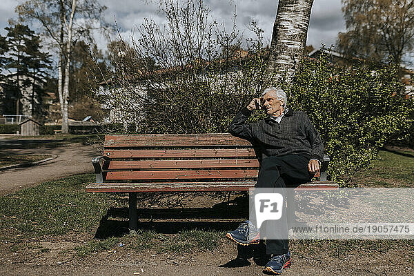 Älterer Mann sitzt auf einer Bank im Park an einem sonnigen Tag
