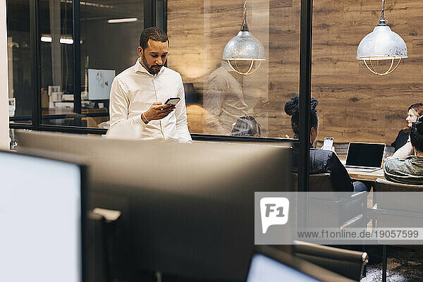 Geschäftsmann mit Smartphone in einem beleuchteten kreativen Büro
