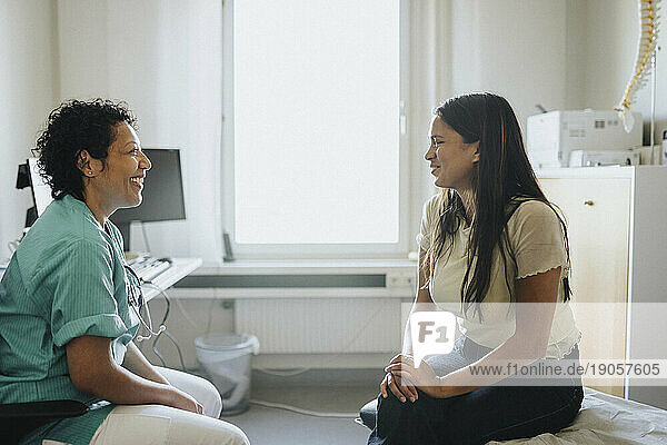 Lächelnder reifer Arzt und weiblicher Patient diskutieren in der Klinik sitzend