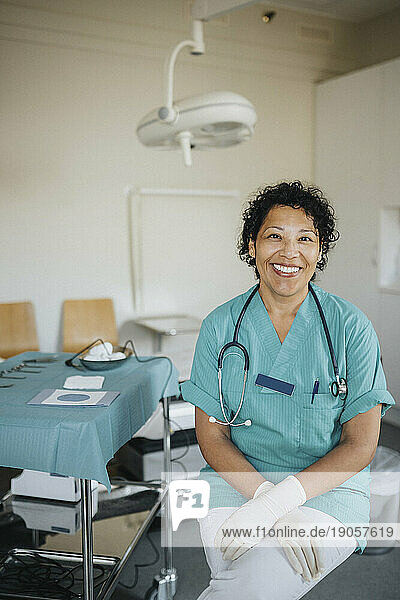 Porträt einer glücklichen Ärztin in medizinischem Kittel  die in einem medizinischen Untersuchungsraum sitzt
