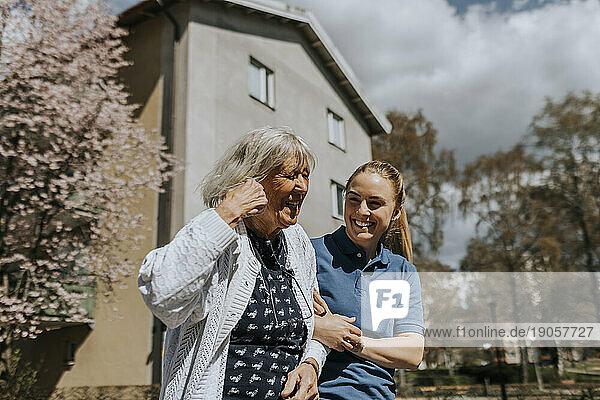 Glückliche Pflegerin mit Arm im Arm einer älteren Frau an einem sonnigen Tag