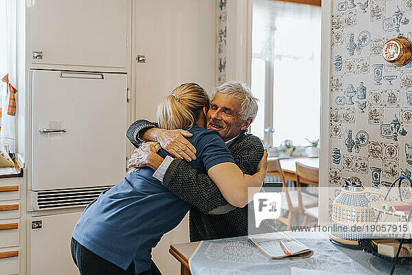 Lächelnder älterer Mann umarmt weibliche Betreuerin zu Hause