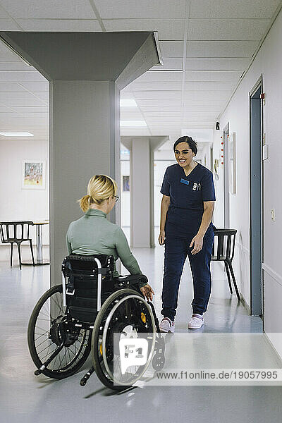 Lächelnde Mitarbeiterin im Gesundheitswesen geht auf einen behinderten Patienten im Krankenhaus zu