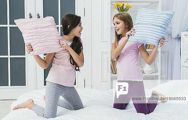 Zwei glückliche weibliche Freunde tun Kissen Kampf Bett nach Hause