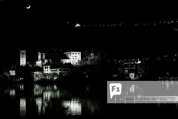 Die Insel San Giulio im Ortasee bei Mondschein und in der Nacht. Häuser und Kirchen vom Gegenufer bilden den Hintergrund