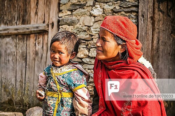Beni  Nepal  ca. Mai 2012: Mutter in rotem Schal und Kopftuch kniet neben ihrer kleinen Tochter mit braunen Haaren und braunen Augen in blau gelber Jacke in Beni  Nepal. Dokumentarischer Leitartikel  Asien
