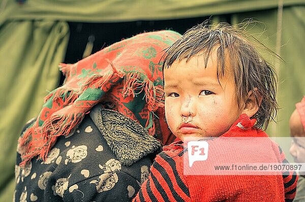 Dolpo  Nepal  ca. Juni 2012: Kleines braunhaariges Mädchen in rotem Pullover schaut mit braunen Augen über die Schulter in die Fotokamera in Dolpo  Nepal. Dokumentarischer Leitartikel  Asien