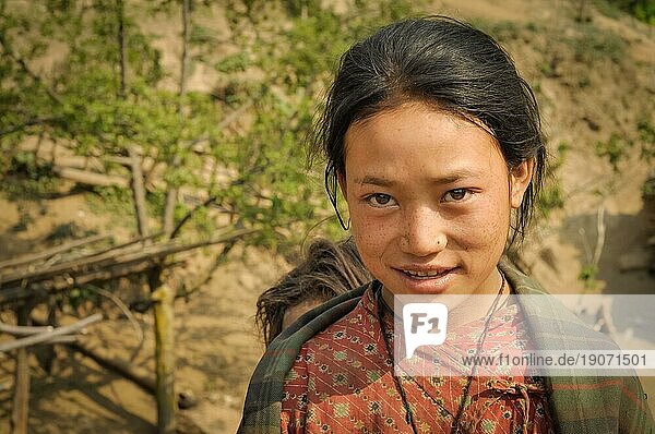 Dolpo  Nepal  ca. Mai 2012: Junges schwarzhaariges Mädchen mit braunen Augen in rotem Hemd lächelt sanft in Dolpo  Nepal. Dokumentarischer Leitartikel  Asien