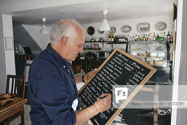 Cafe owner writing menu on black board with pen