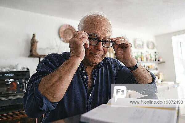 Smiling cafe owner wearing eyeglasses and looking at diary in coffee shop