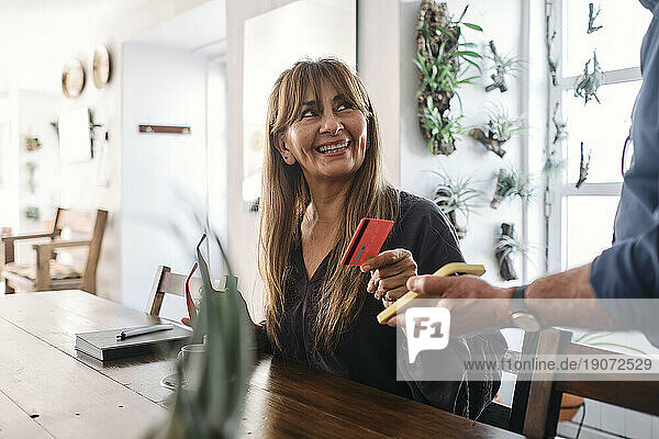 Smiling senior woman paying with credit card on smart phone