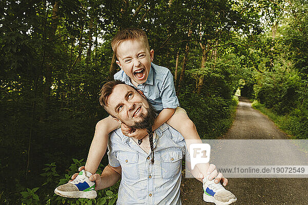 Playful father carrying son on shoulder at forest