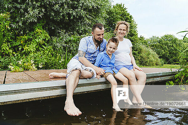 Pregnant woman spending leisure time with family sitting on footbridge over lake