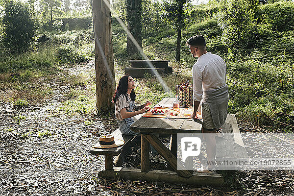 Young couple enjoying food on bench in forest