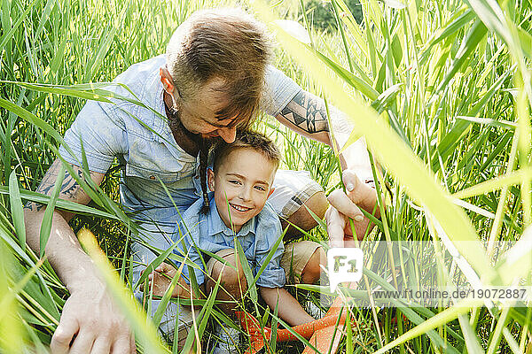 Father and son playing with toy airplane on grassy field