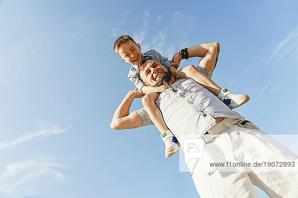Father carrying son on shoulder on sunny day