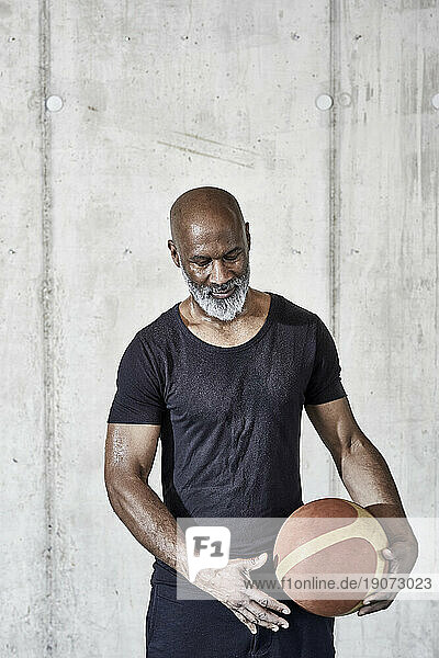 Mature man holding basketball at concrete wall