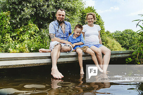 Happy family spending leisure time sitting on footbridge over lake