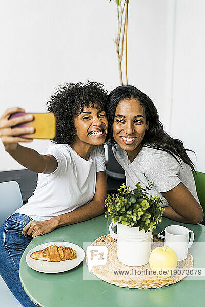 Two happy girlfriends sitting at table taking a selfie
