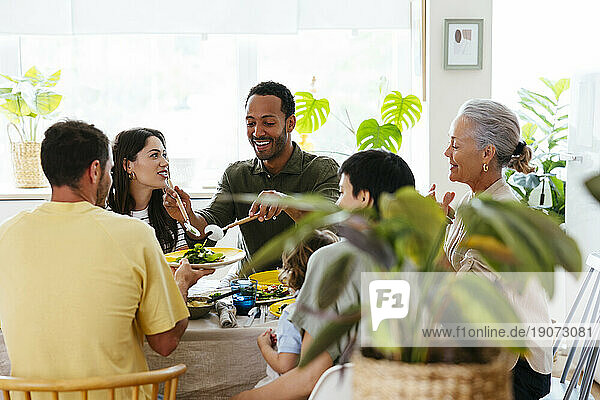 Smiling man serving salad to family at dining table at kitchen