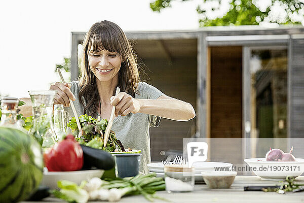Smiling woman preparing a salad on garden table