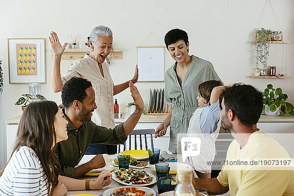 Smiling family giving high-five on dining table in kitchen