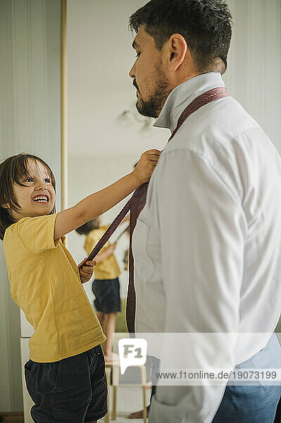 Smiling son adjusting father's necktie at home