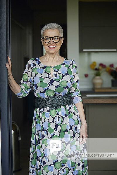 Portrait of smiling senior woman wearing patterned dress at balcony door