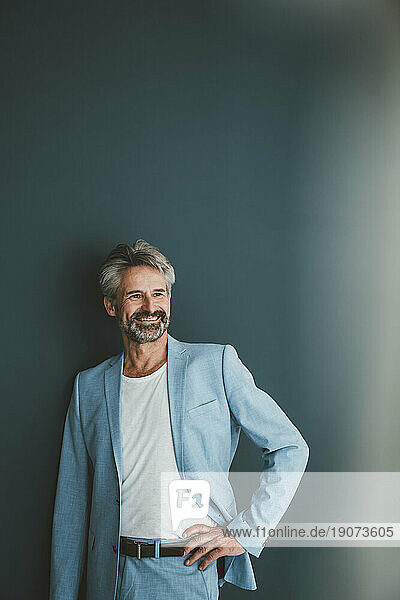 Smiling businessman with hand on hip against teal background