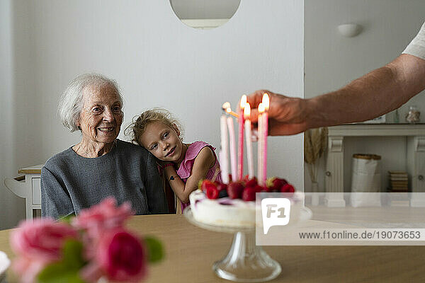 Father lighting birthday candles with family at home