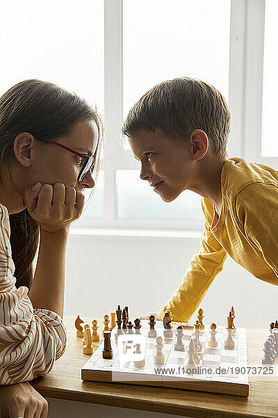 Smiling boy looking and playing chess with mother at home