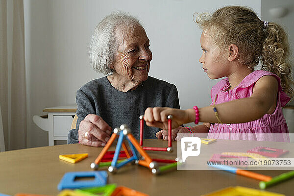 Smiling grandmother and granddaughter playing leisure game at home