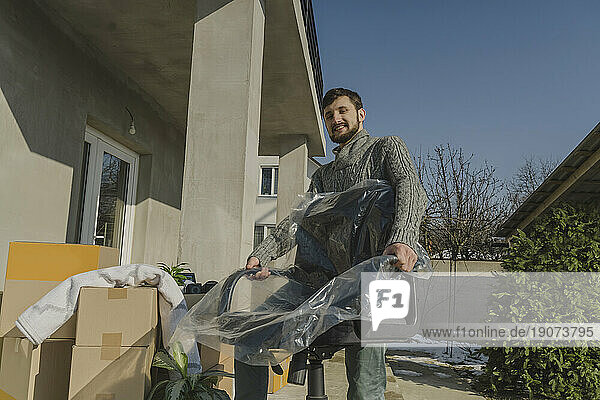 Smiling man carrying wrapped chair into new house